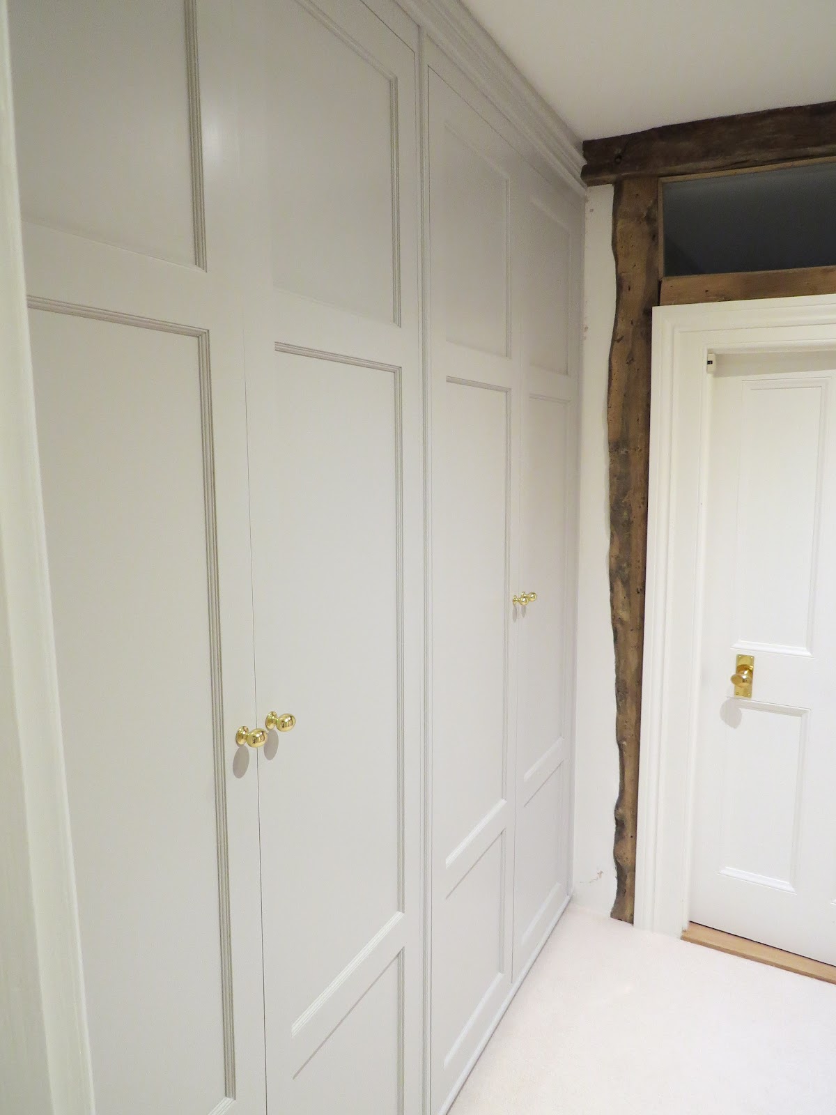 White-painted fitted cupboards beside an exposed timber beam — bespoke joinery by Reeve & Co, Debenham, Suffolk